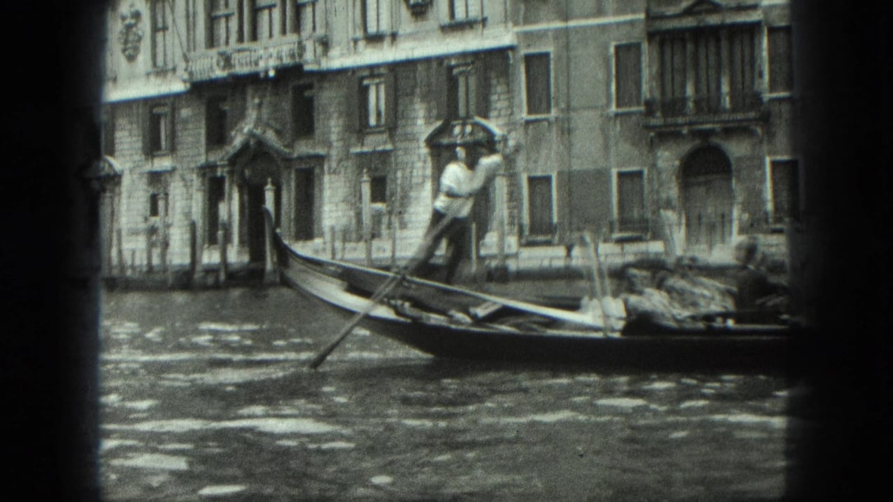 Gondolier stands in a gondola near a canal building with arched doorway and windows.