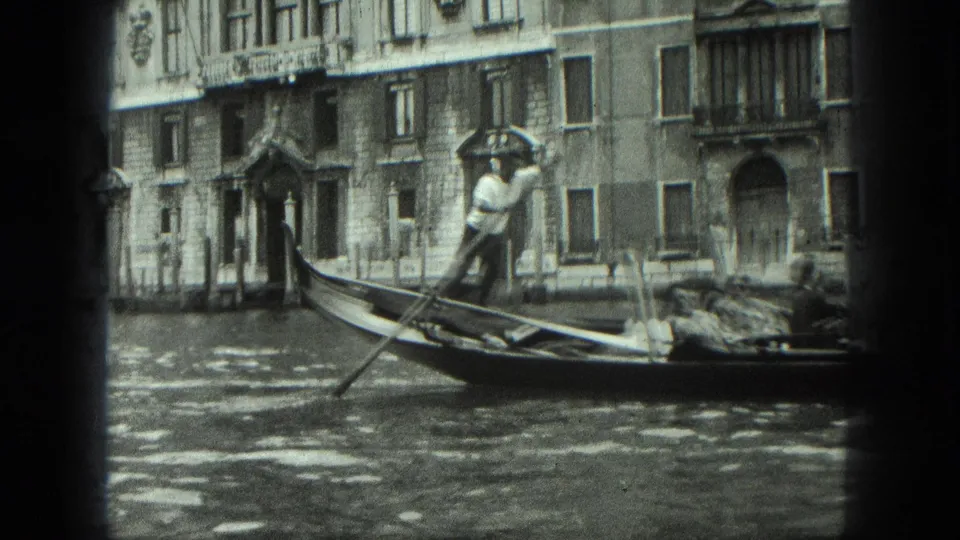 1975 Venice frame with the gondolier visible at the stern as the gondola moves along the canal in front of historic-looking facades.