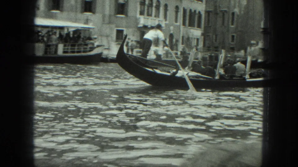 1975 8mm Venice footage shows a gondolier using a long oar as passengers ride past waterfront buildings.
