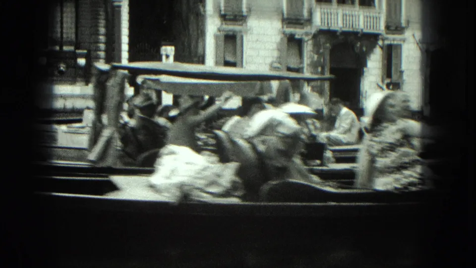 1975 Venice canal view with seated passengers in a gondola and architectural facades in the background.