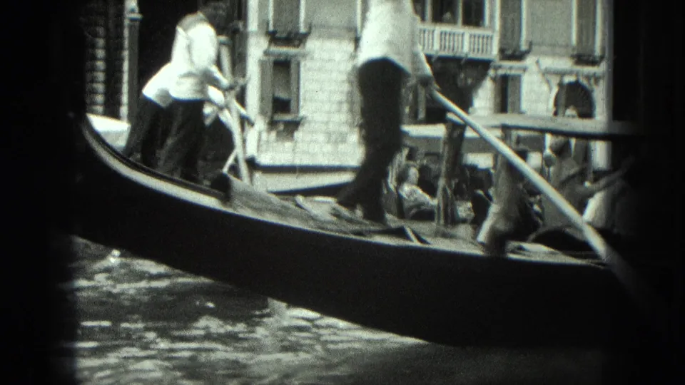 1975 Venice 8mm frame showing gondoliers in light shirts maneuvering a gondola on the canal.