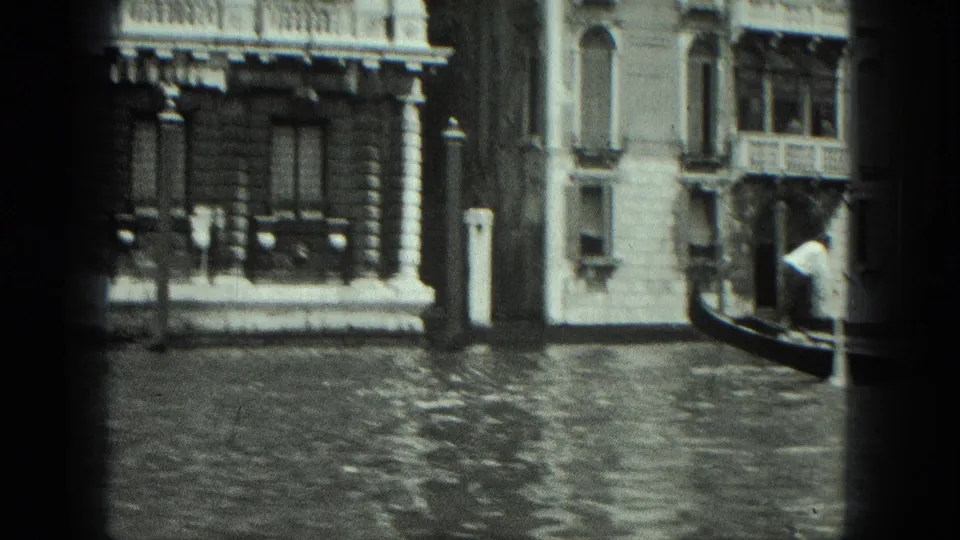 A handheld 1975 Venice canal frame shows palazzi, rippled water, striped poles, and part of a gondola at the edge.