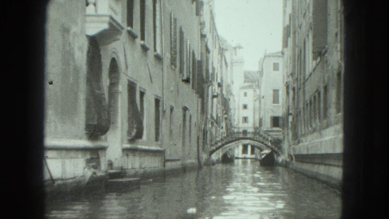 Narrow Venetian canal between tall buildings with a small arched bridge in the distance.