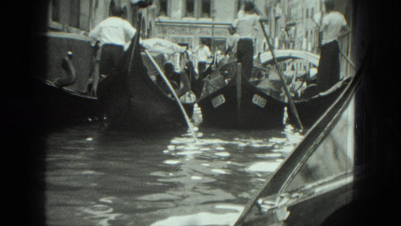 Gondoliers guide crowded boats along a narrow canal with a bridge in the distance.