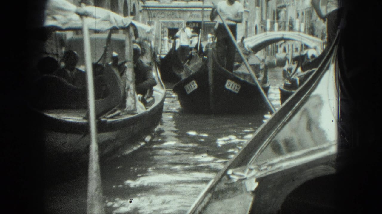 1975 Venice canal view with several gondolas, seated tourists, gondoliers, water reflections, and old buildings in soft 8mm black-and-white.