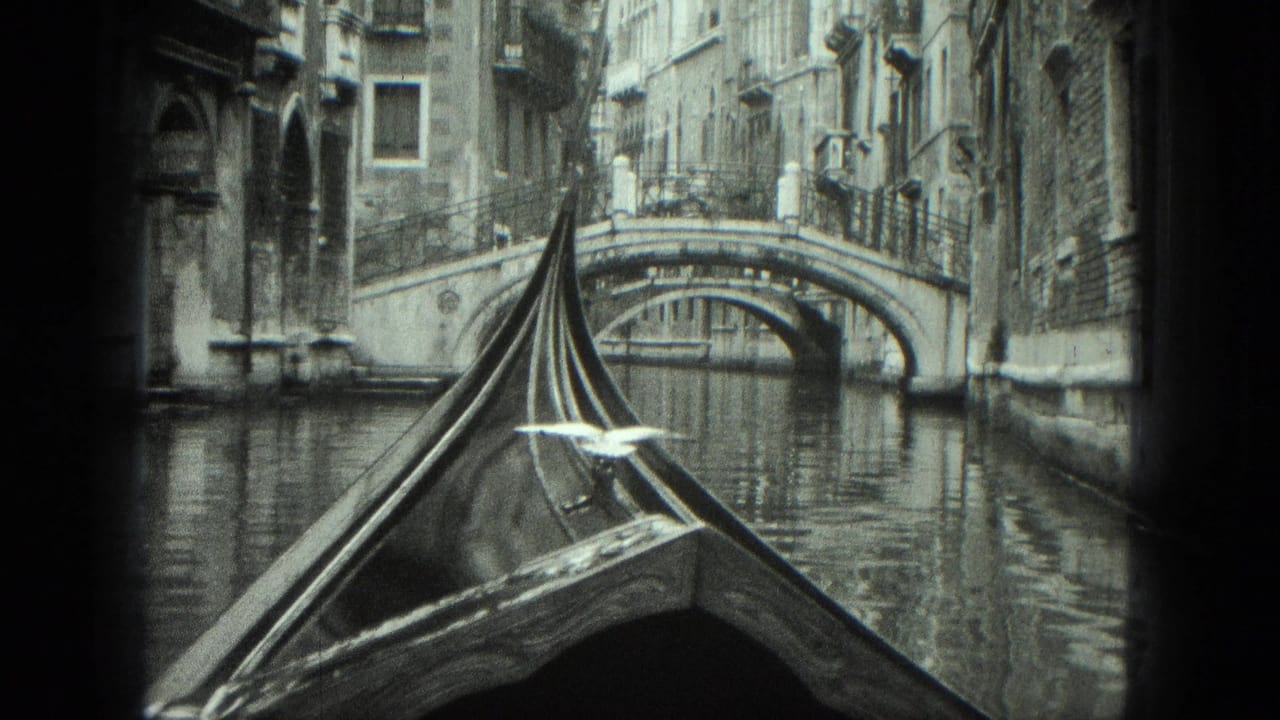 Gondola prow moving along a narrow canal toward an arched stone bridge.