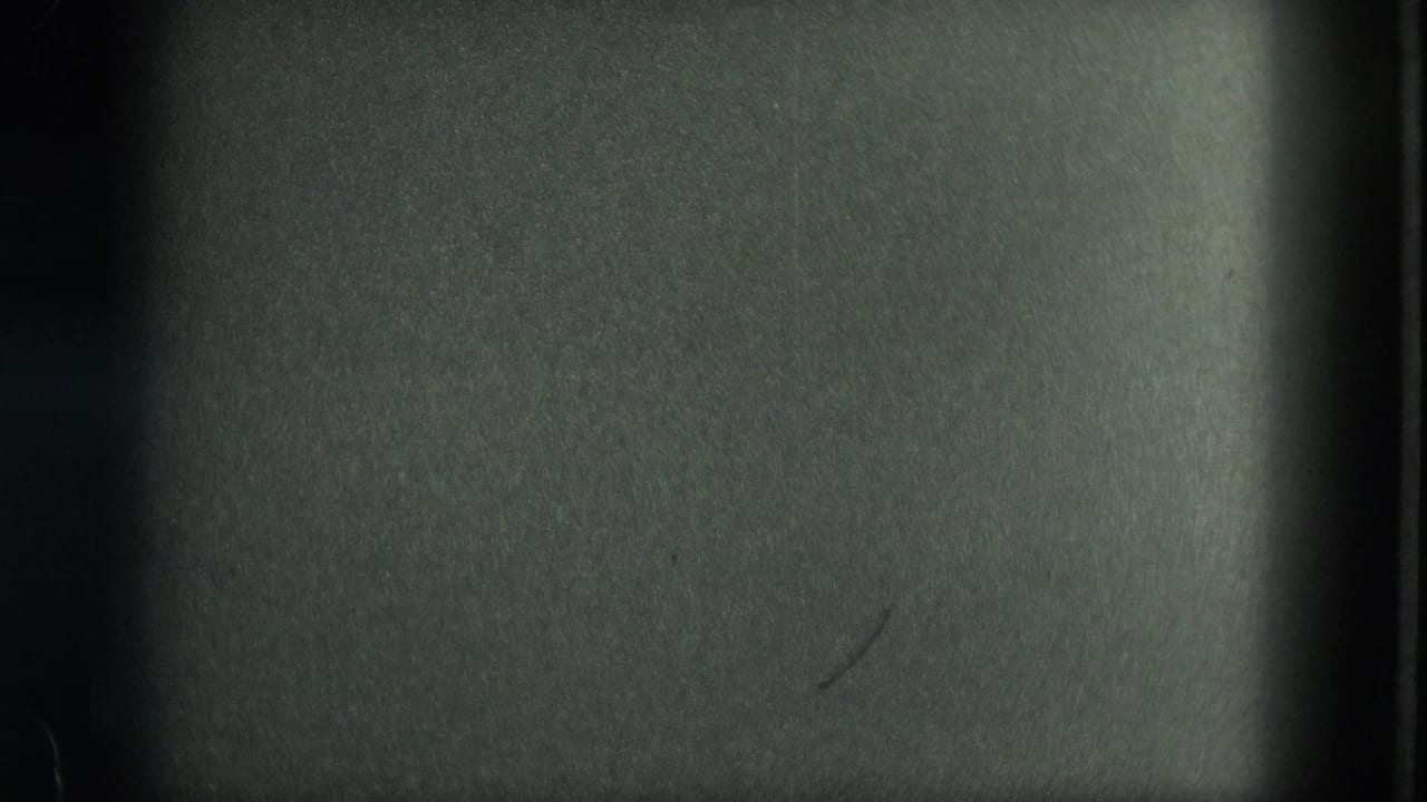 Dark 8mm frame from the Venice clip, showing mostly underexposed film surface and gate edges before the canal view appears.