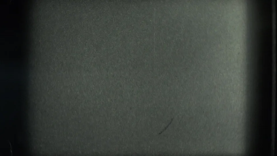 Dark 8mm frame from the Venice clip, showing mostly underexposed film surface and gate edges before the canal view appears.