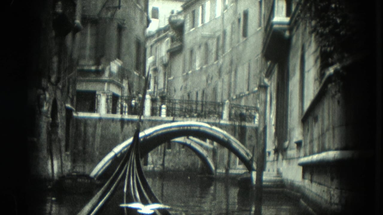 1975 8mm Venice view from a gondola moving toward a low arched bridge between tall canal-side buildings.