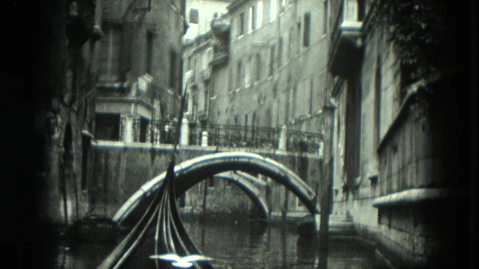 1975 8mm Venice view from a gondola moving toward a low arched bridge between tall canal-side buildings.