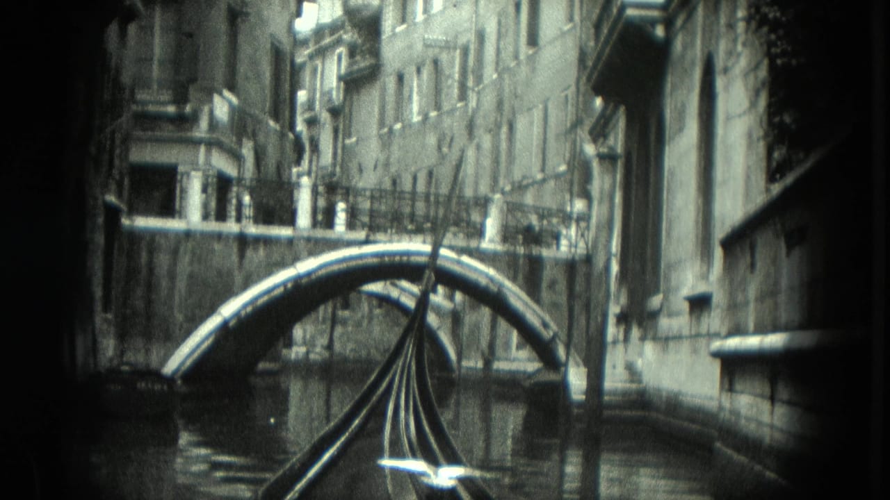 Gondola prow passes closer to the arched bridge between canal buildings.