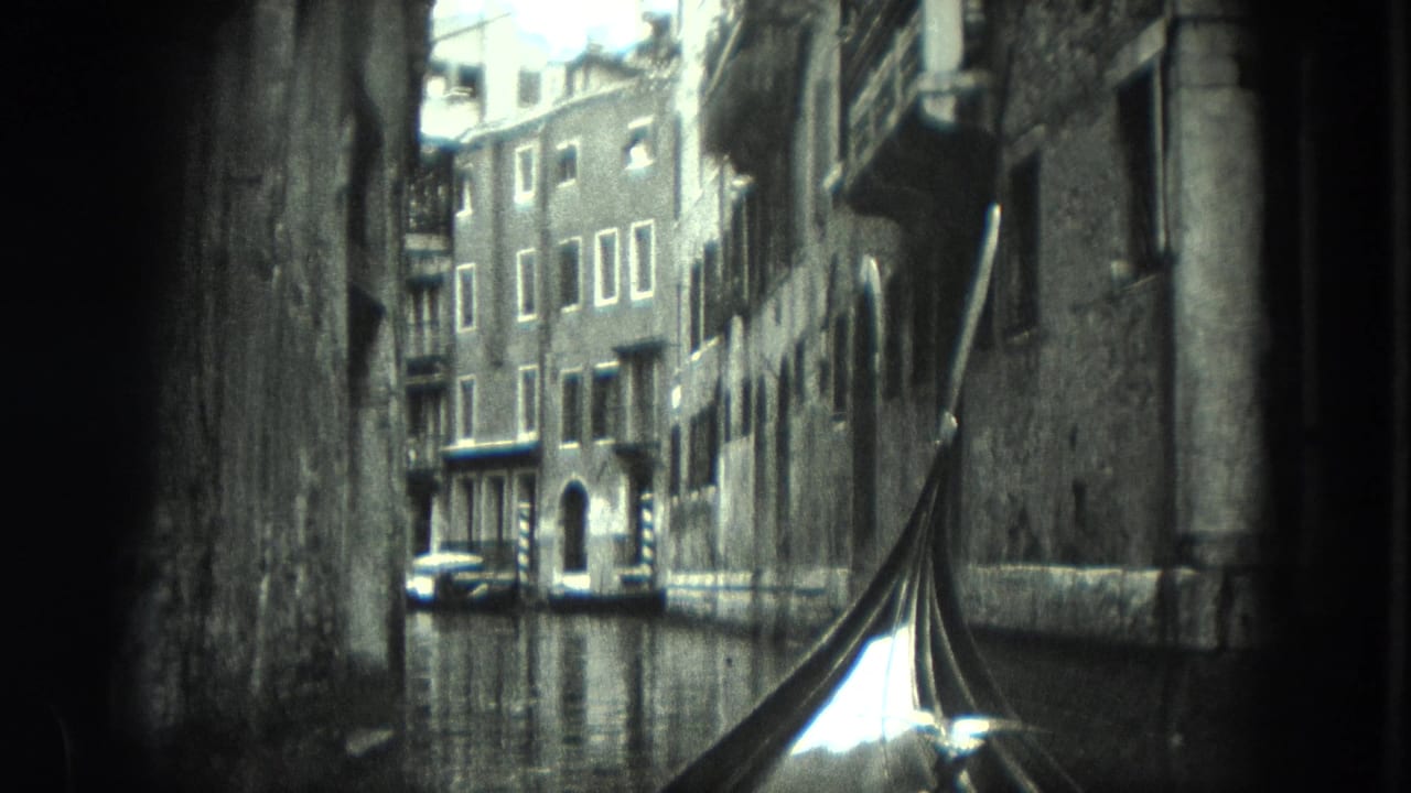 Gondola prow in a narrow canal with old buildings and a small boat ahead.