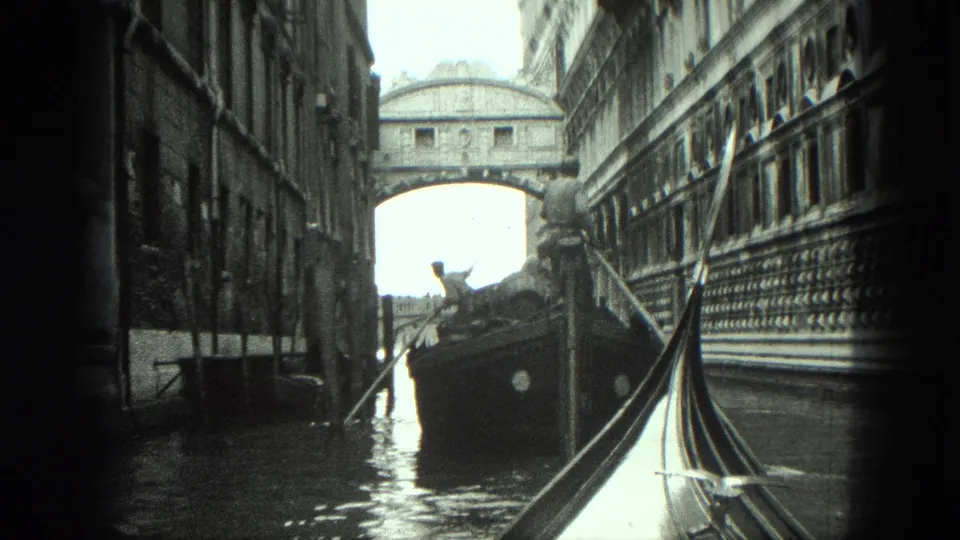 Black-and-white 8mm Venice frame showing a gondola view toward the Bridge of Sighs, with a boat and tall canal-side buildings.