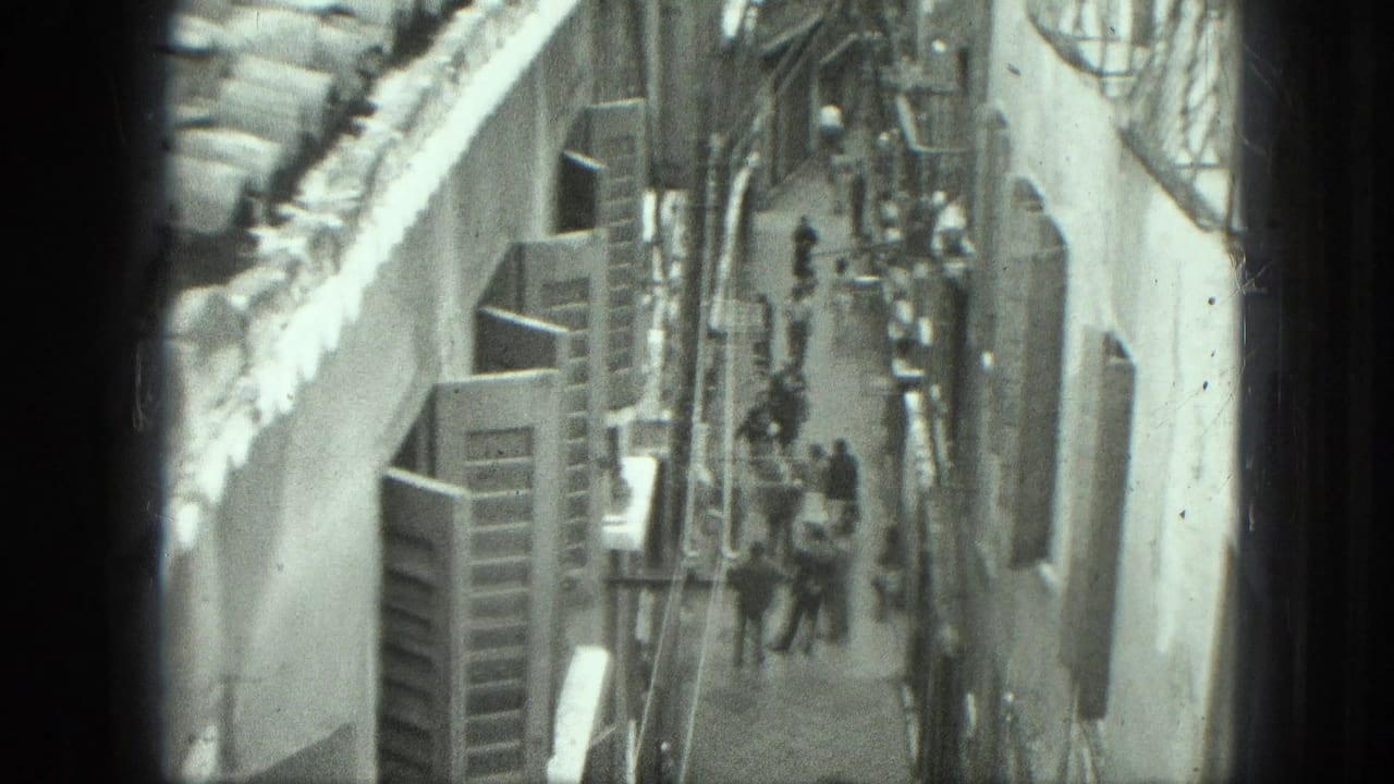 High-angle view down a narrow alley with pedestrians between tall buildings.