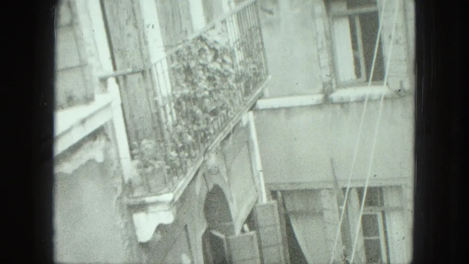 1975 Venice home-movie frame showing a pale residential facade with balcony railing, plants, windows, and soft handheld framing.