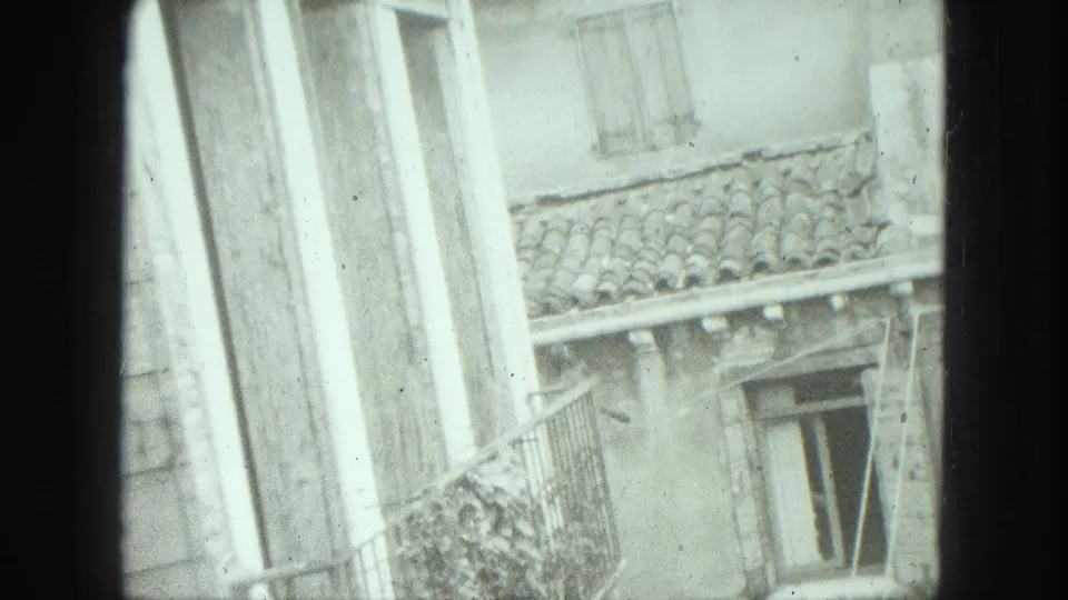 1975 Venice home-movie frame showing weathered exterior walls, shuttered windows, a balcony rail, and clay roof tiles.