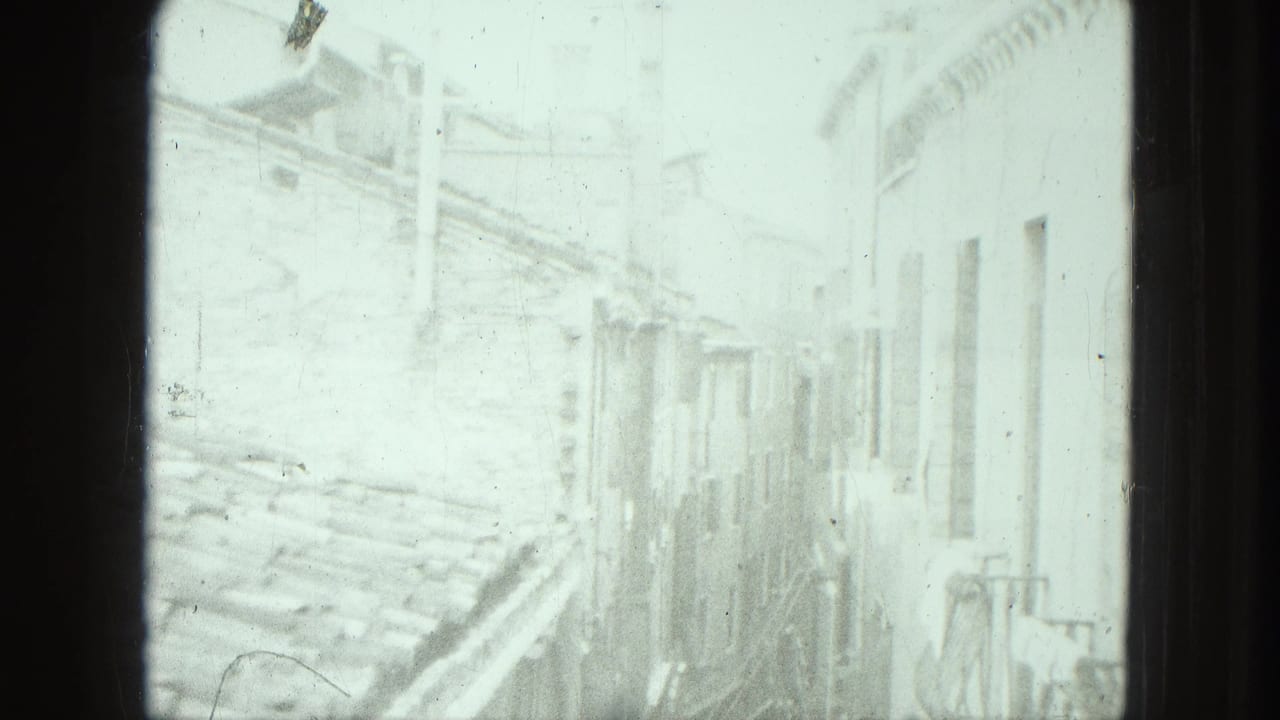 High-angle 8mm frame of a sunlit narrow street in Venice, with old building walls and little pedestrian detail visible.
