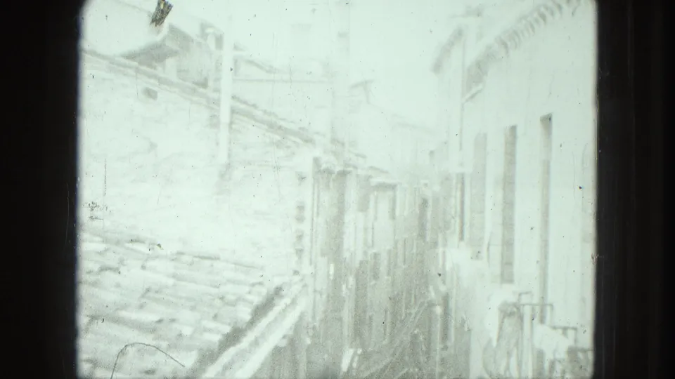 High-angle 8mm frame of a sunlit narrow street in Venice, with old building walls and little pedestrian detail visible.