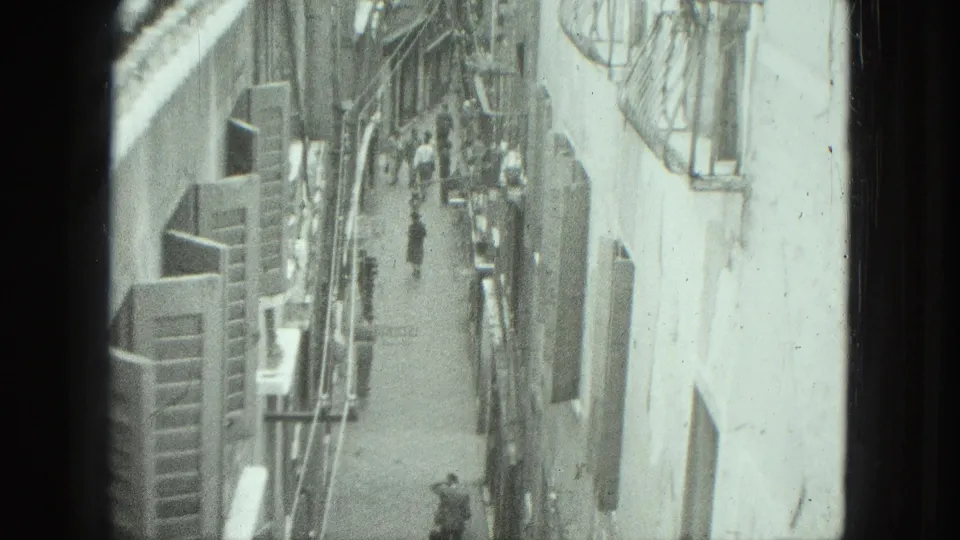 Elevated 1975 Venice street view with pedestrians moving through a narrow alley lined by tall buildings and shutters.