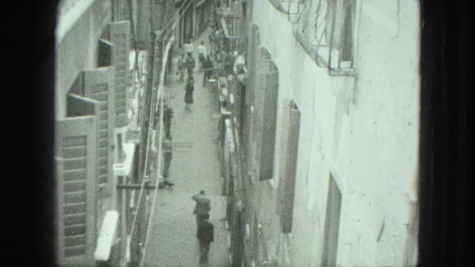 High-angle 1975 Venice frame showing a person walking away in a narrow alley, with several pedestrians farther along the street.