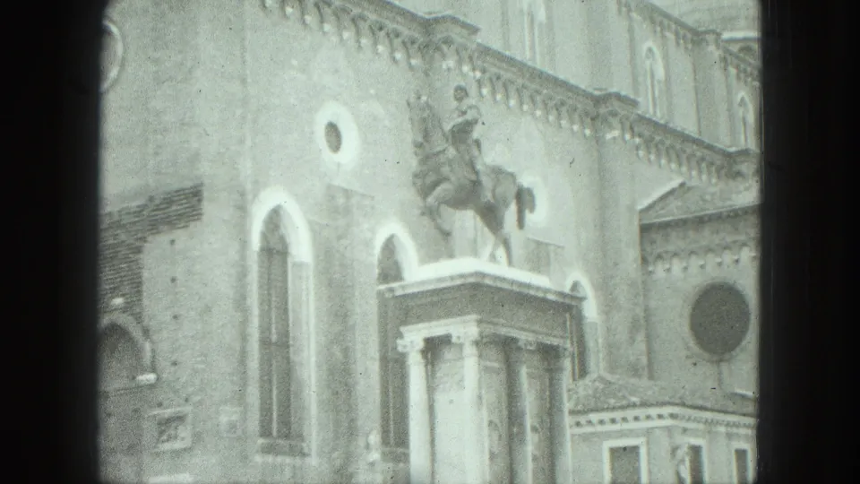 1975 Venice home-movie frame centered on a public equestrian monument with surrounding arched stonework.