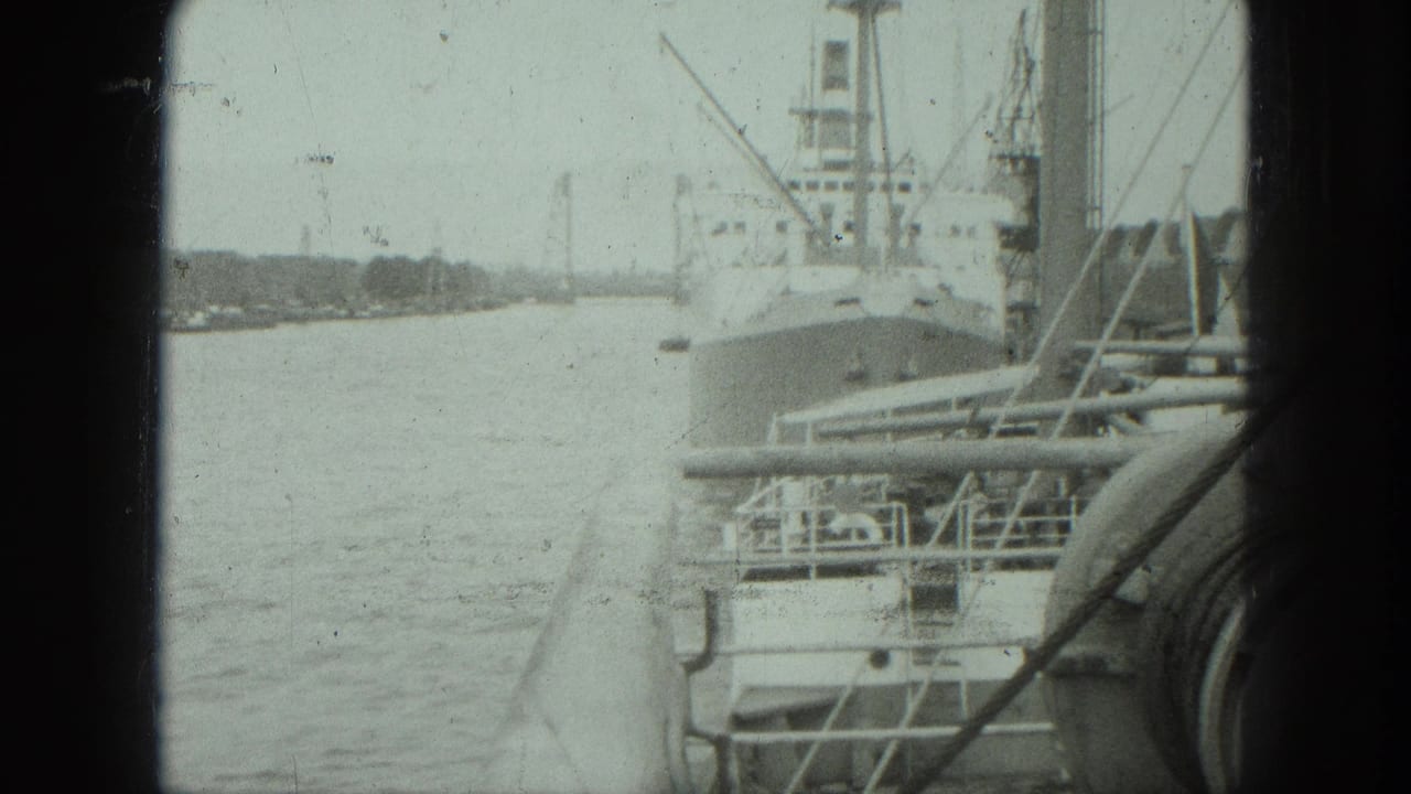 Cargo ship docked beside harbor water, seen past a dark window edge and railings.