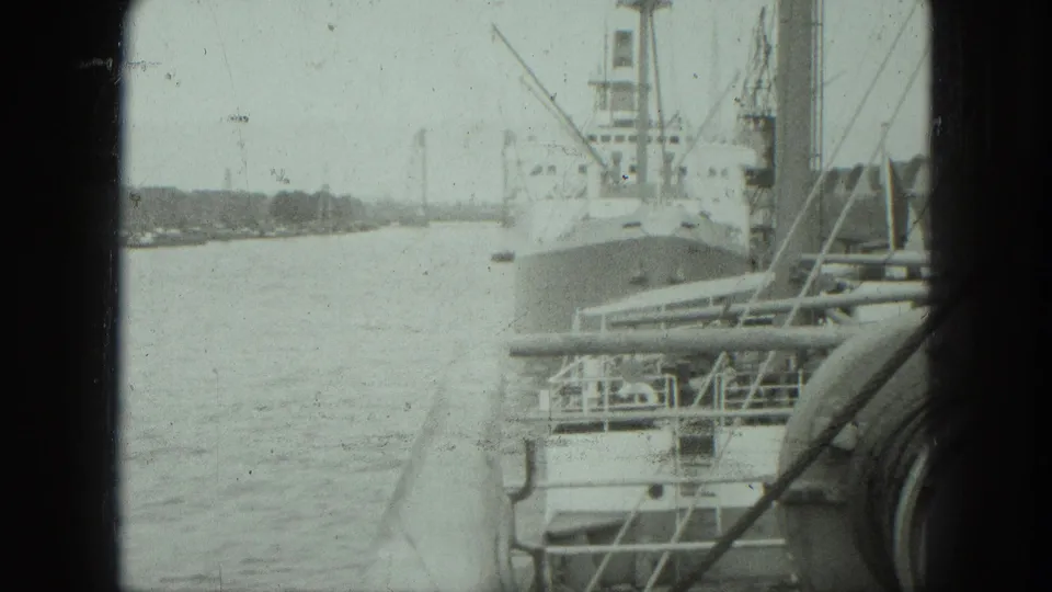 1975 Venice harbor view on 8mm film, with a docked cargo ship, calm water, cranes, and dark frame edges.