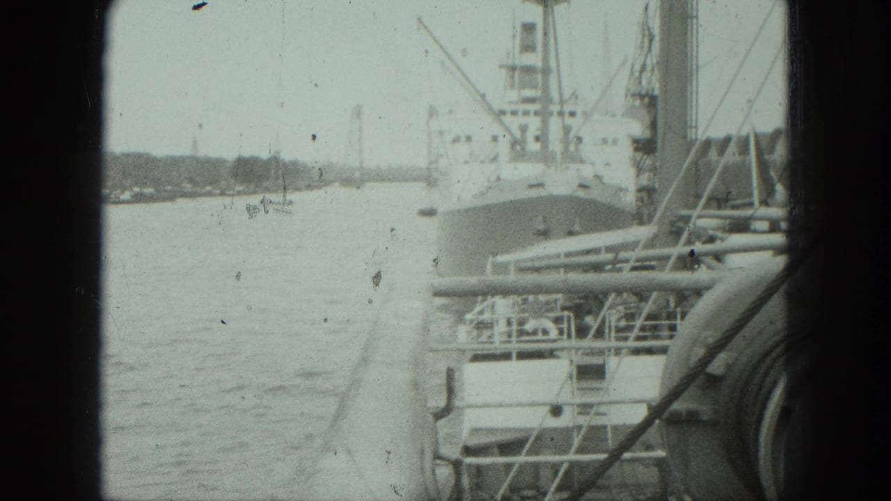 Docked cargo ship and harbor water with cranes and rigging in the background.