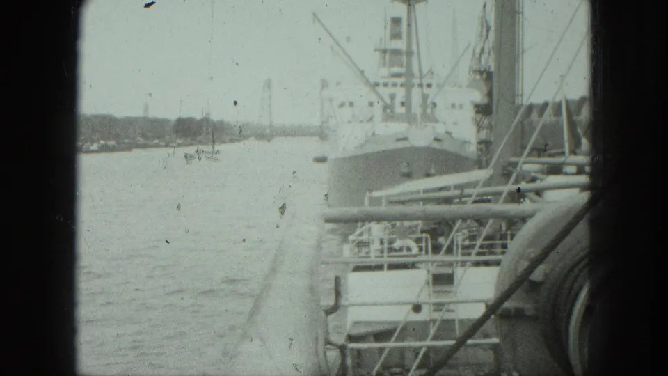 1975 Venice waterfront frame showing a cargo ship at port, harbor water, cranes, rigging, and film scratches.