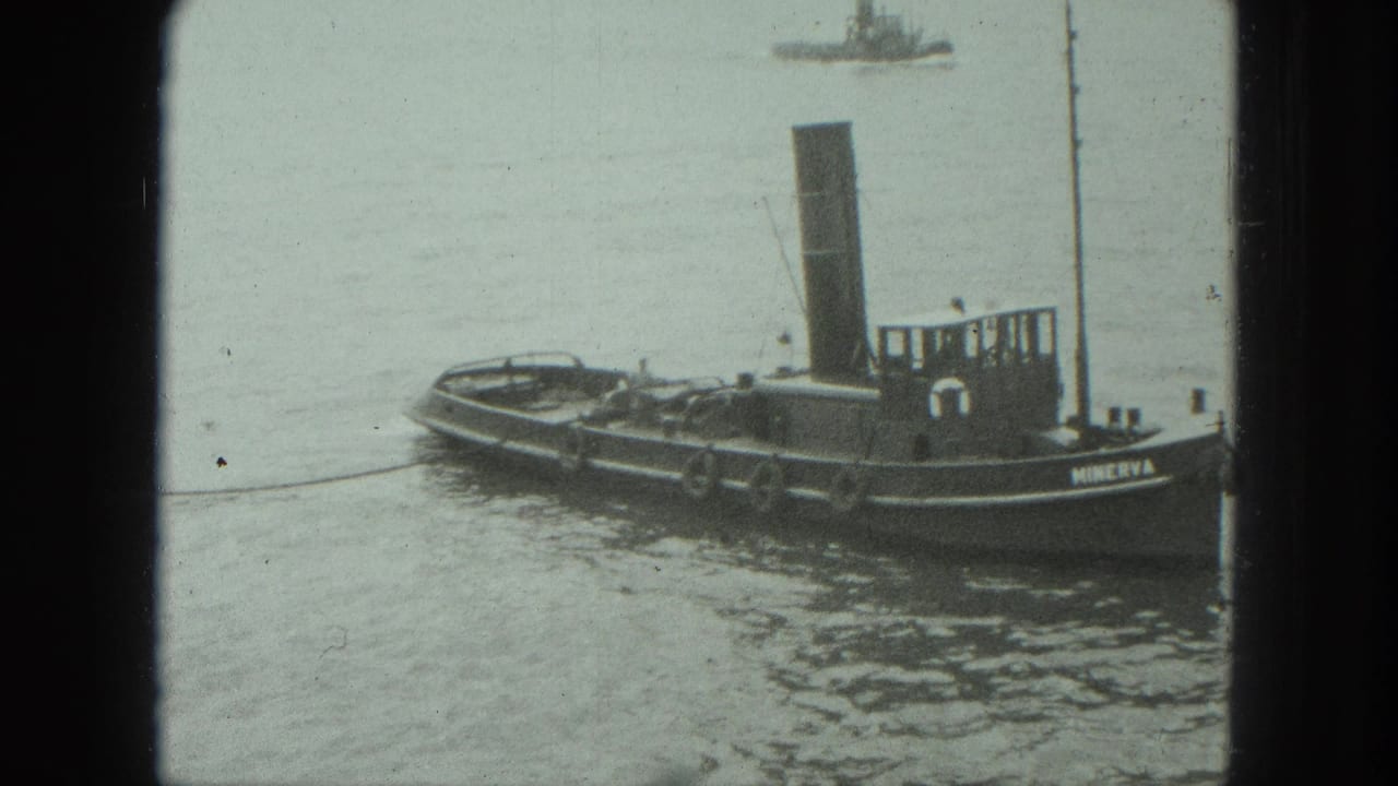 Small steam tugboat named Minerva floating on calm water, seen through dark film-frame borders.