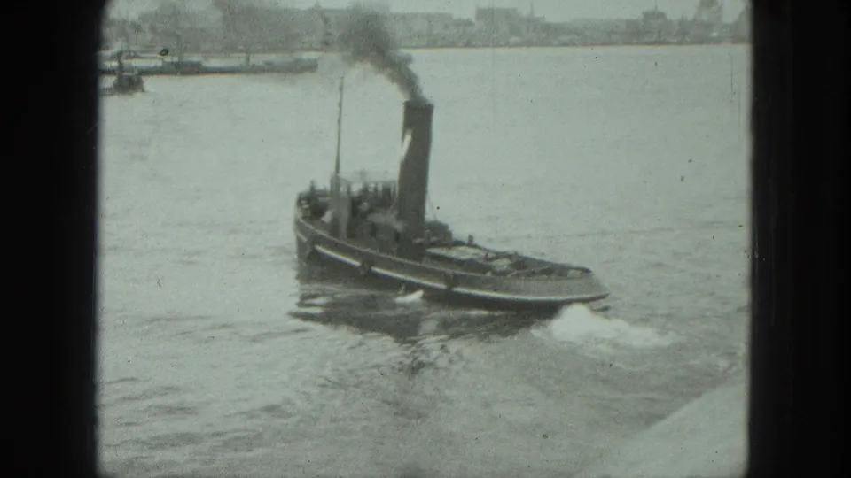 1975 Venice 8mm frame of the small tugboat underway, its smokestack emitting a dark plume over calm water.