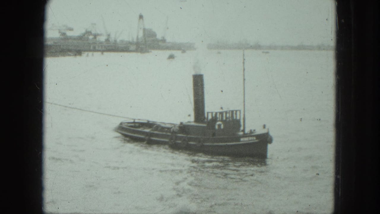 Small tugboat moving across calm water with industrial shoreline in the distance.