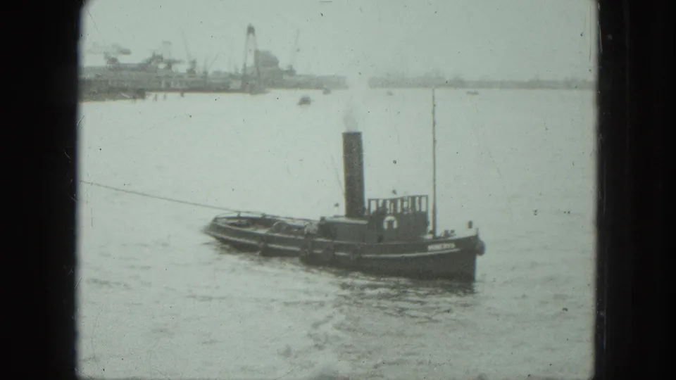 1975 Venice 8mm frame showing a small tugboat with a tall smokestack on calm water near a hazy industrial port.