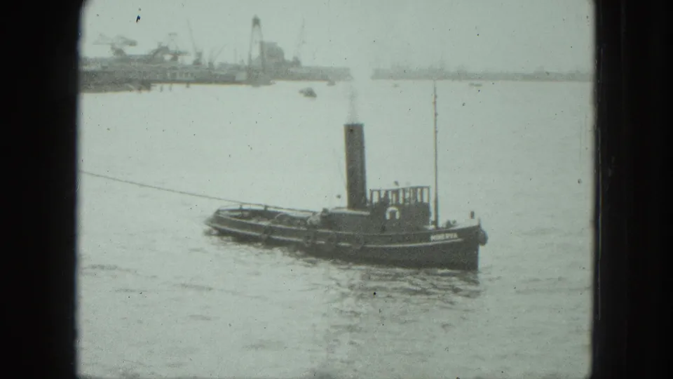 1975 Venice home-movie frame of a tugboat seen in profile against calm water and a distant industrial waterfront.