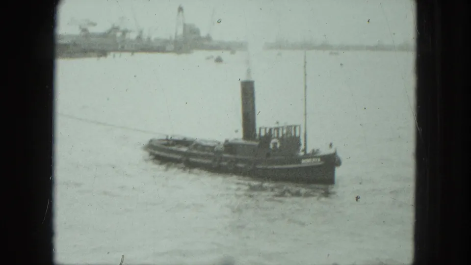 1975 Venice 8mm frame showing the tugboat lower in the frame, with calm water and a soft industrial shoreline beyond.