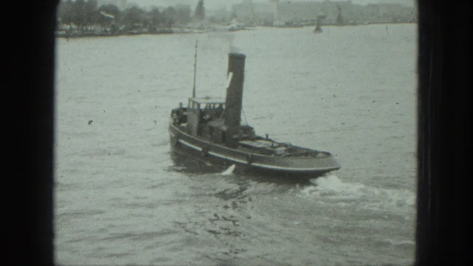 1975 Venice home-movie frame showing the tugboat from behind as it turns away and leaves a small wake.
