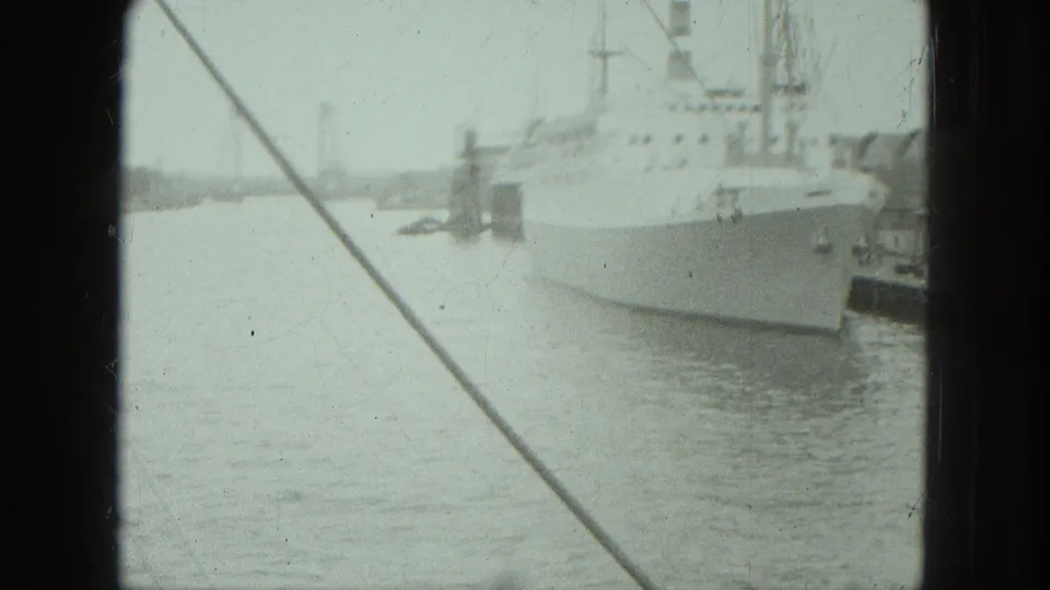 Large ocean liner moored in Venice harbor, filmed from behind a dark ship or window frame with rigging crossing the view.