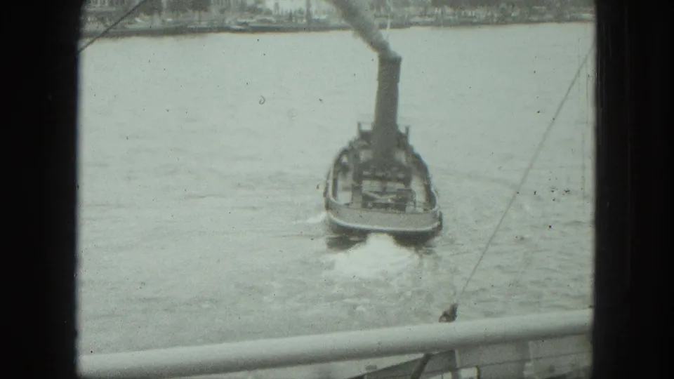 A small dark boat with a tall smokestack moves through Venice harbor water, seen from above with railing and rigging in the 8mm frame.