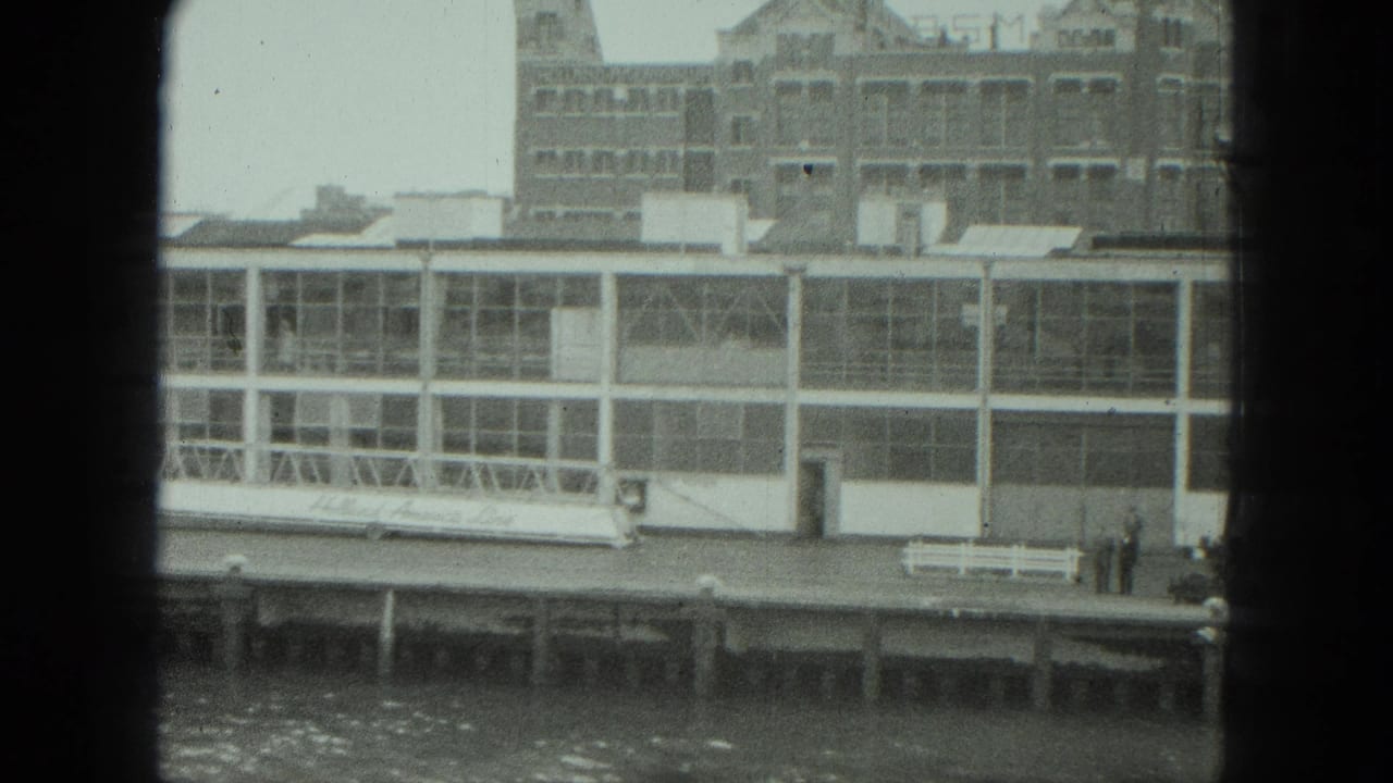 Dockside glass structure with a white bench and two small figures near the pier edge.
