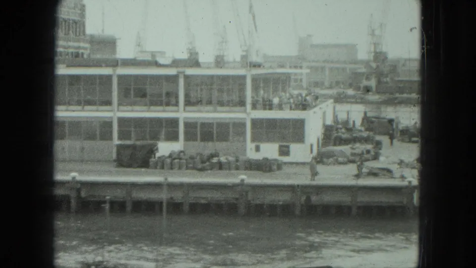 Venice waterfront in 1975 showing people near a modern dock building, with harbor cranes and water visible beyond the window frame.