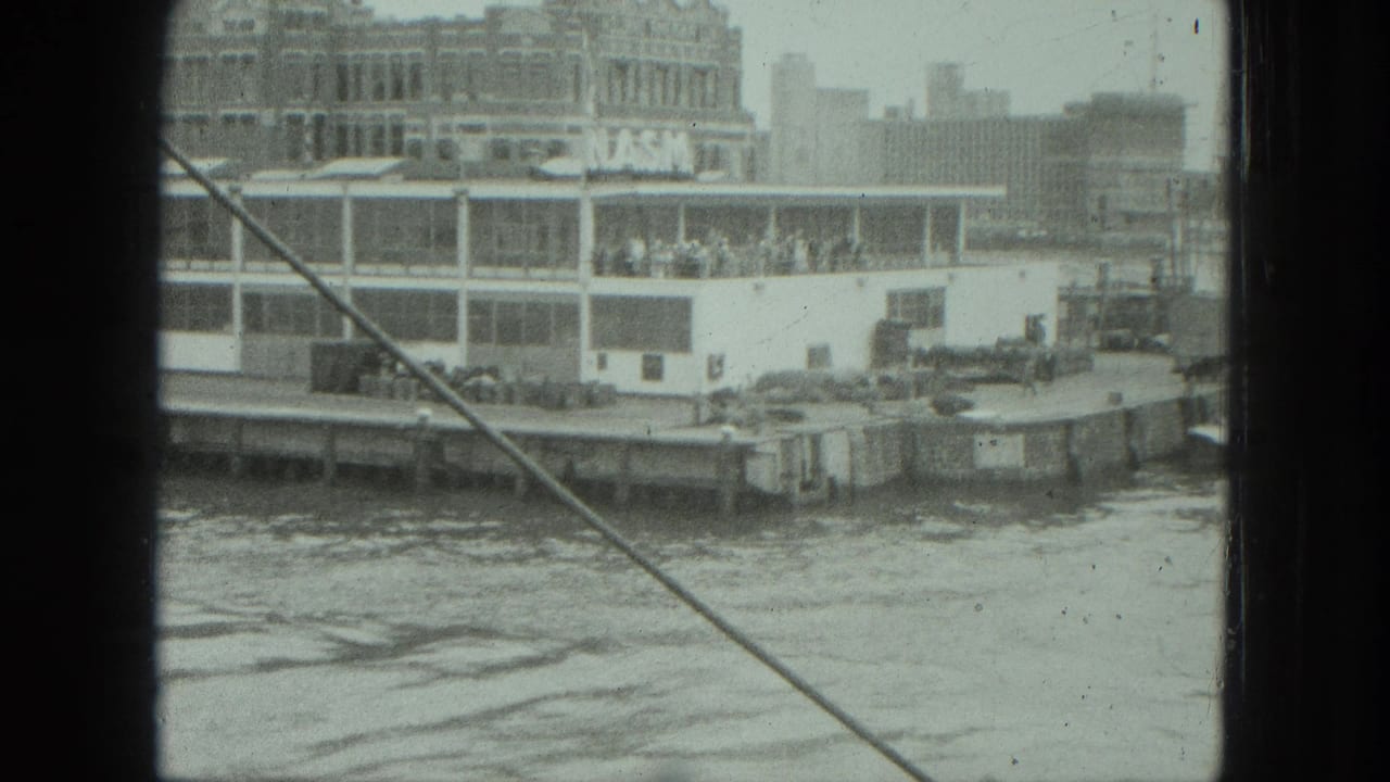 Waterfront passenger boat docked beside buildings, seen through dark boat framing and a diagonal cable.