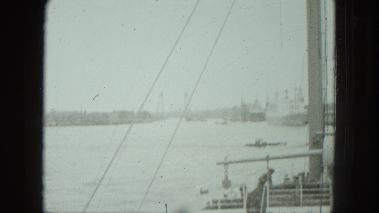 1975 Venice harbor view through a window, with water, a small boat, pier railings, and distant shoreline structures.