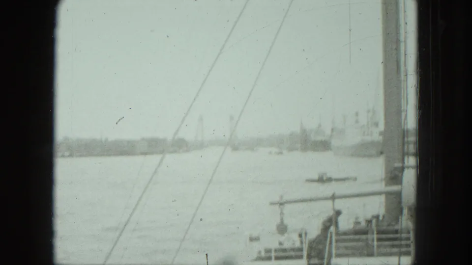 1975 Venice harbor view through a window, with water, a small boat, pier railings, and distant shoreline structures.