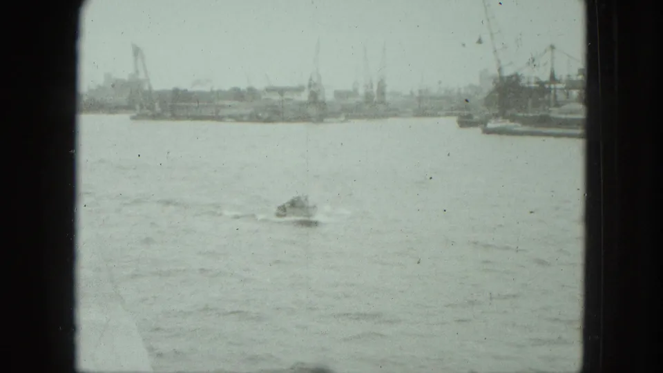 1975 Venice harbor frame showing a small boat crossing open water, with cranes and dockside structures in the background.