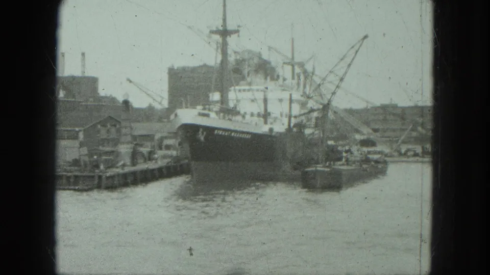 1975 Venice harbor view of a large docked ship beside pier structures, cranes, waterfront buildings, and moving water.