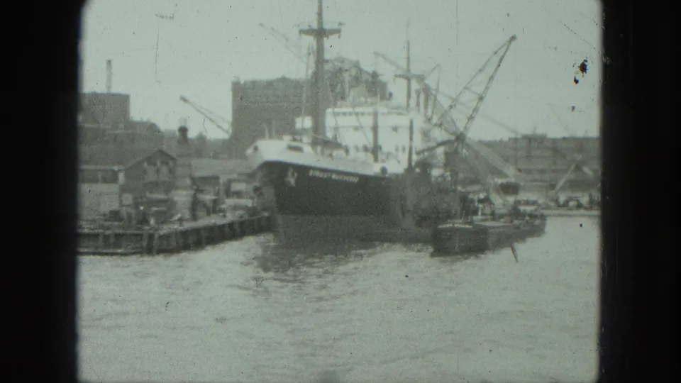 1975 Venice harbor view showing a moored cargo ship, dock structures, cranes, and water in soft 8mm footage.