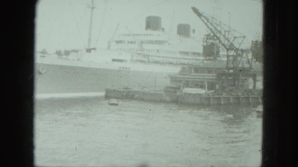1975 Venice harbor view with a large white passenger-style ship, dock cranes, small boats, and hazy water foreground.
