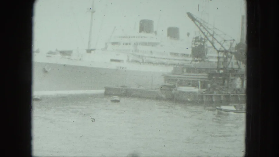 1975 Venice waterfront frame showing a large white vessel, crane equipment, small craft, and pale 8mm harbor water.