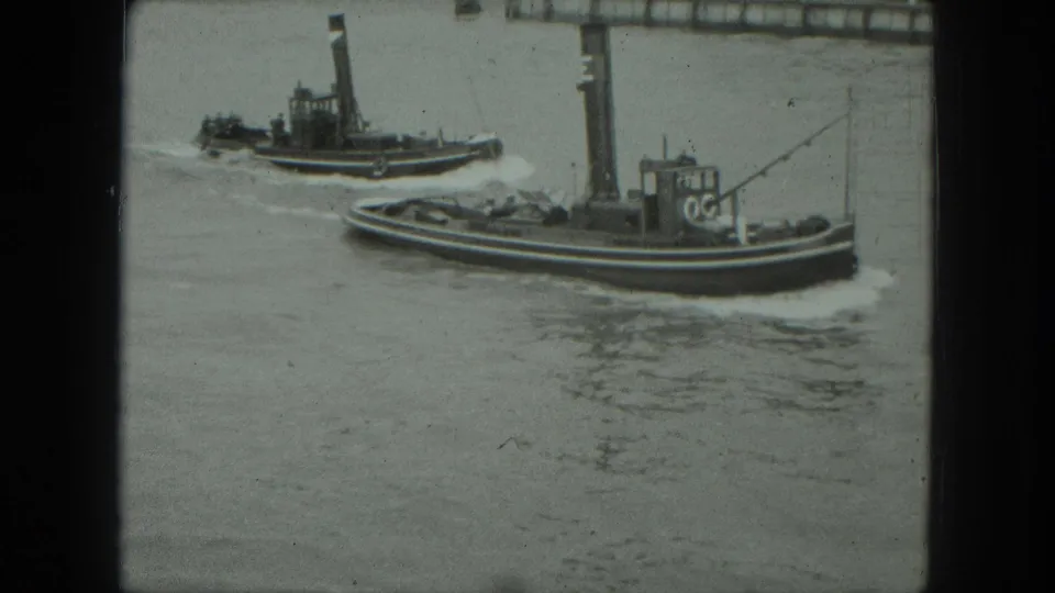 1975 8mm Venice frame showing two tugboats traveling on a broad waterway near the waterfront.