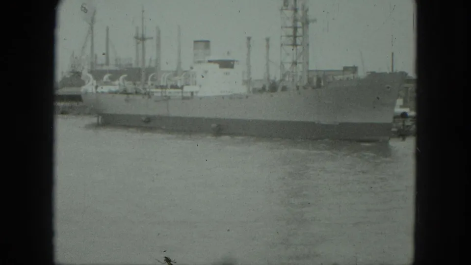 A static 1975 Venice harbor frame shows a large ship at the quay, water in the foreground, and industrial waterfront forms behind it.